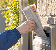 新聞配達員が郵便受けへ新聞を投函するイメージ